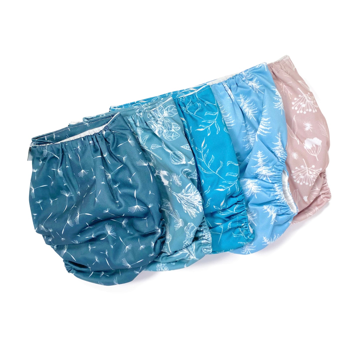 A set of five reusable nappies, made from 100% recycled polyester. The included nappies are: Wild Lilac, Cool Pines, Blue Fern, Blue Harvest and Midnight Breeze. View shows all five nappies back facing, in a diagonal line.