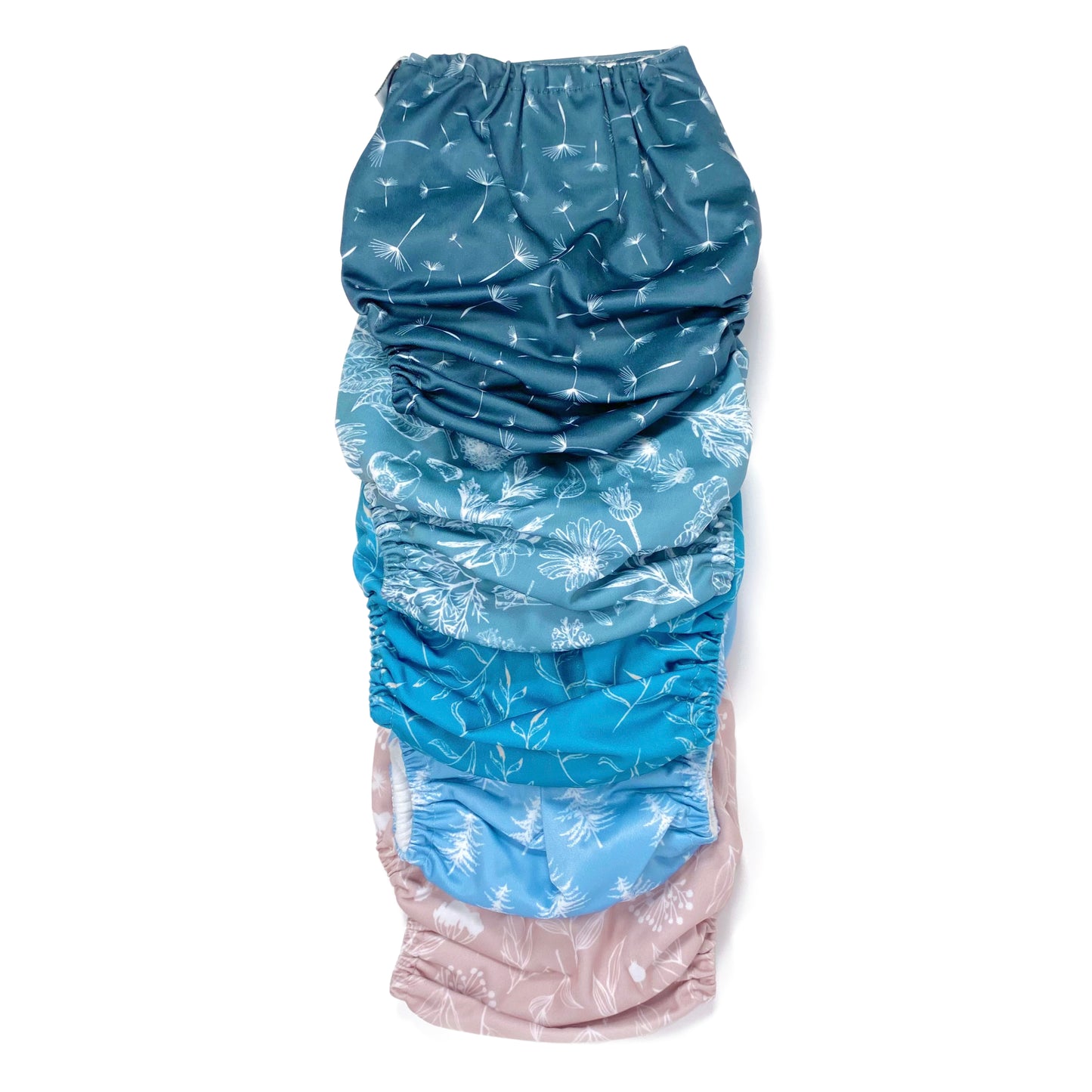 A set of five reusable nappies, made from 100% recycled polyester. The included nappies are: Wild Lilac, Cool Pines, Blue Fern, Blue Harvest and Midnight Breeze. View shows all five nappies back facing, in a vertical line.