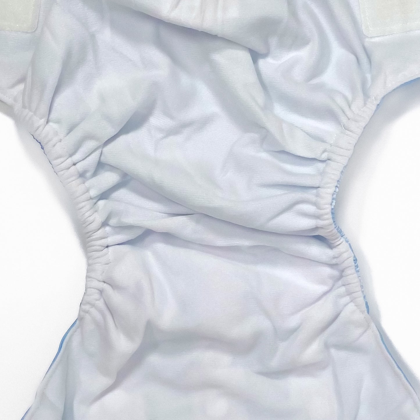 An adjustable reusable nappy for babies and toddlers, featuring a cool blue pine design design, with images of white pine trees on a blue background. Image shows a zoomed in view of the nappy fabric lining.