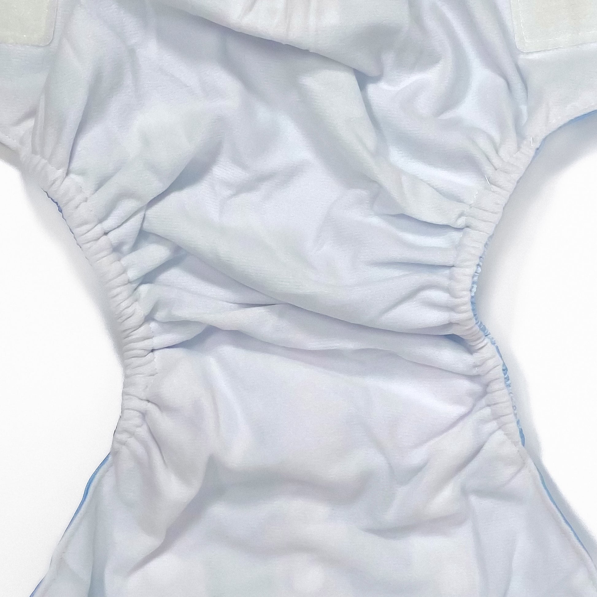 An adjustable reusable nappy for babies and toddlers, featuring a cool blue pine design design, with images of white pine trees on a blue background. Image shows a zoomed in view of the nappy fabric lining.