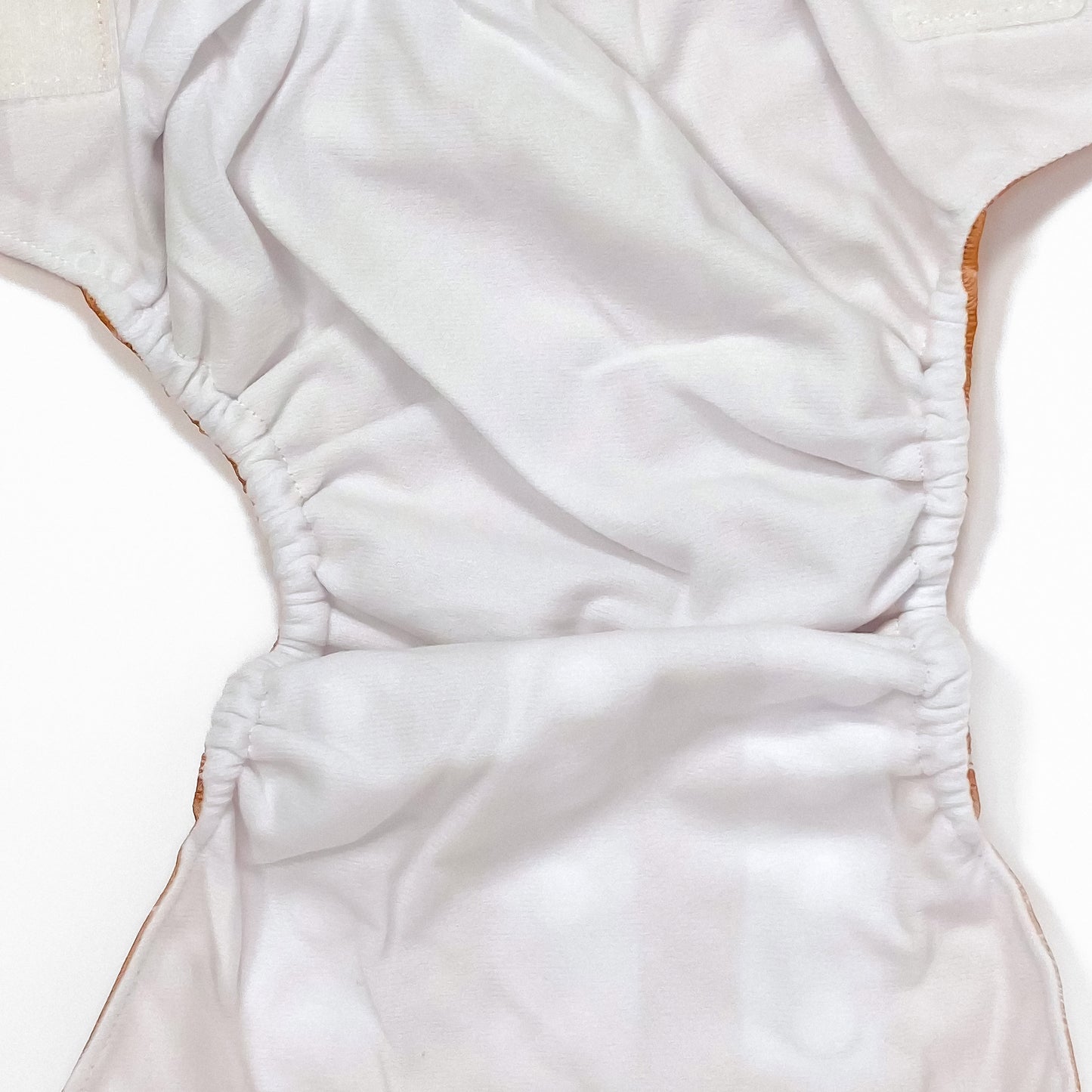 An adjustable reusable nappy for babies and toddlers, featuring a floral copper design, with floral images on a copper background. Image shows a zoomed in view of the nappy fabric lining.