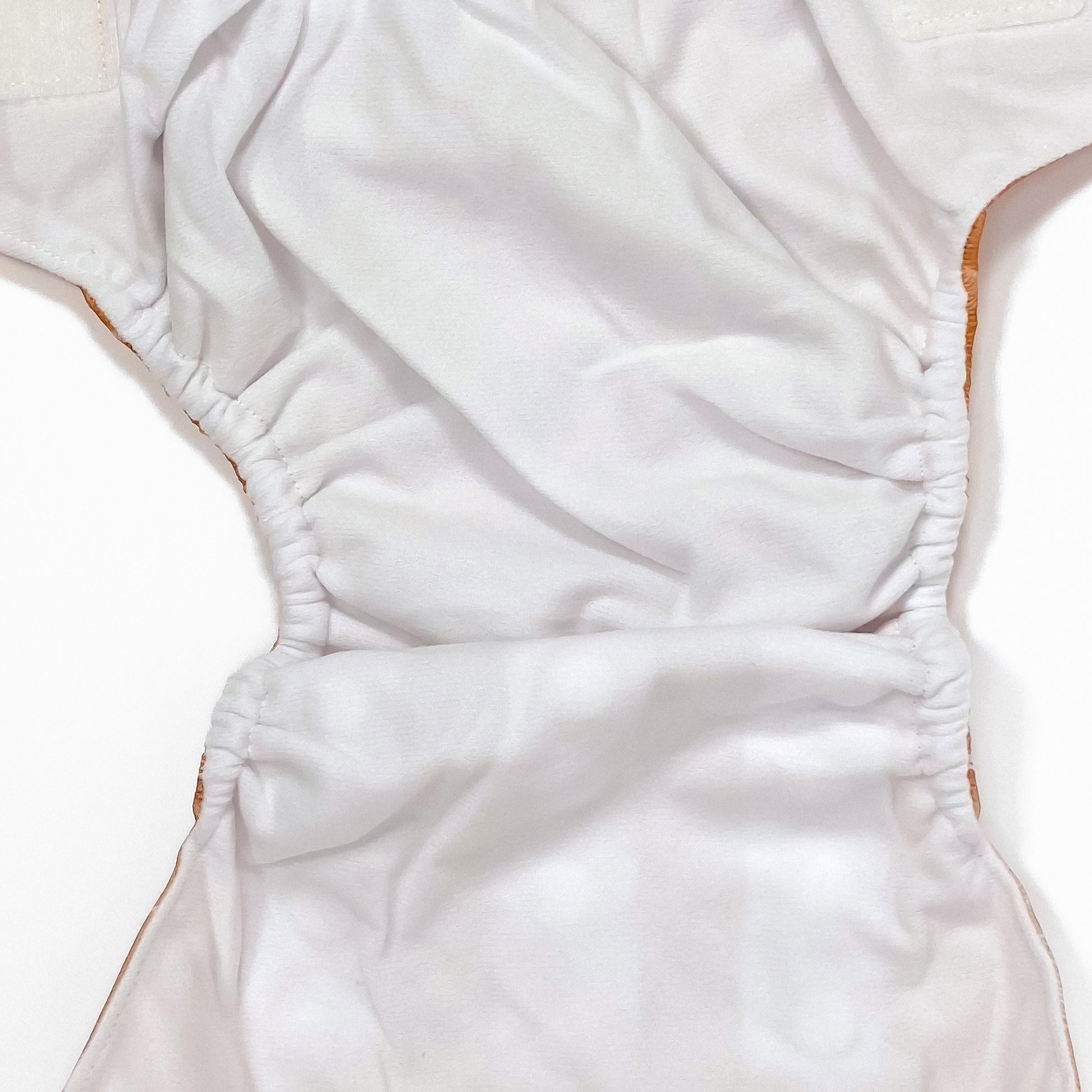 An adjustable reusable nappy for babies and toddlers, featuring a floral copper design, with floral images on a copper background. Image shows a zoomed in view of the nappy fabric lining.