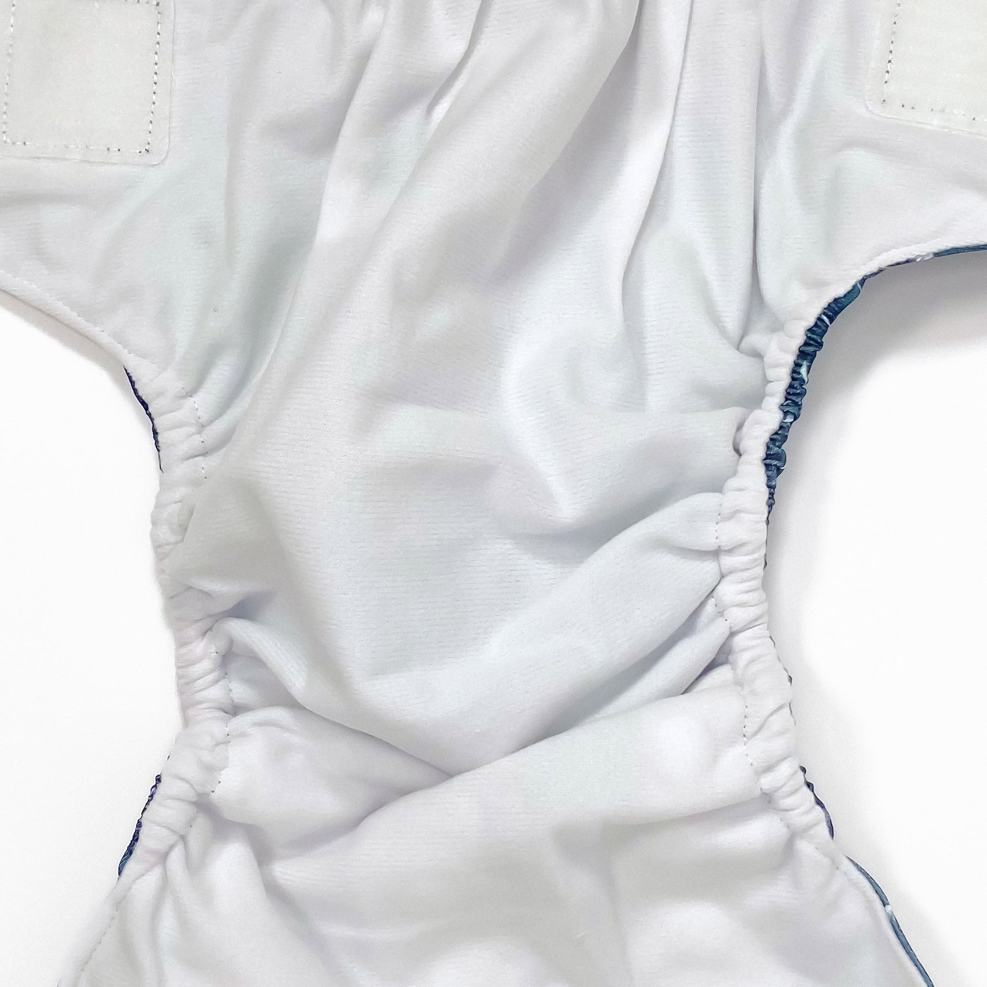 An adjustable reusable nappy for babies and toddlers, featuring a midnight breeze design, with images of dandelion seeds on a navy blue background. Image shows a zoomed in view of the nappy fabric lining.