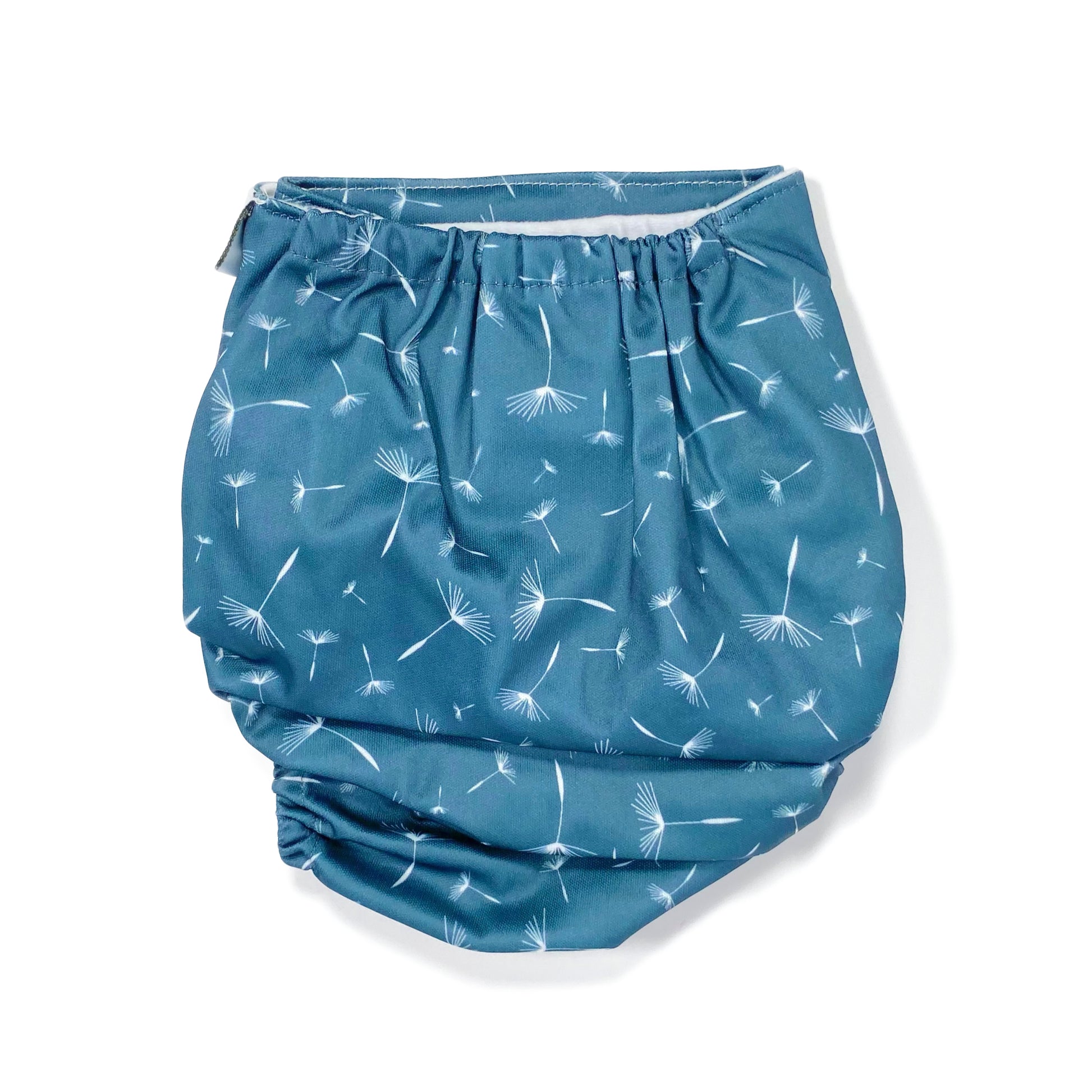 An adjustable reusable nappy for babies and toddlers, featuring a midnight breeze design, with images of dandelion seeds on a navy blue background. View shows the back of the nappy.