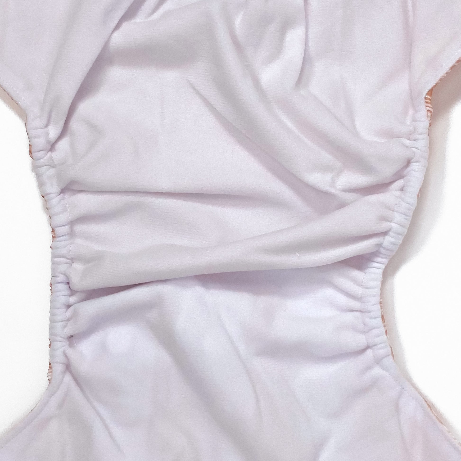 An adjustable reusable nappy for babies and toddlers, featuring a peach rainbow design, with images of white rainbows on a peach background. Image shows a zoomed in view of the nappy fabric lining.