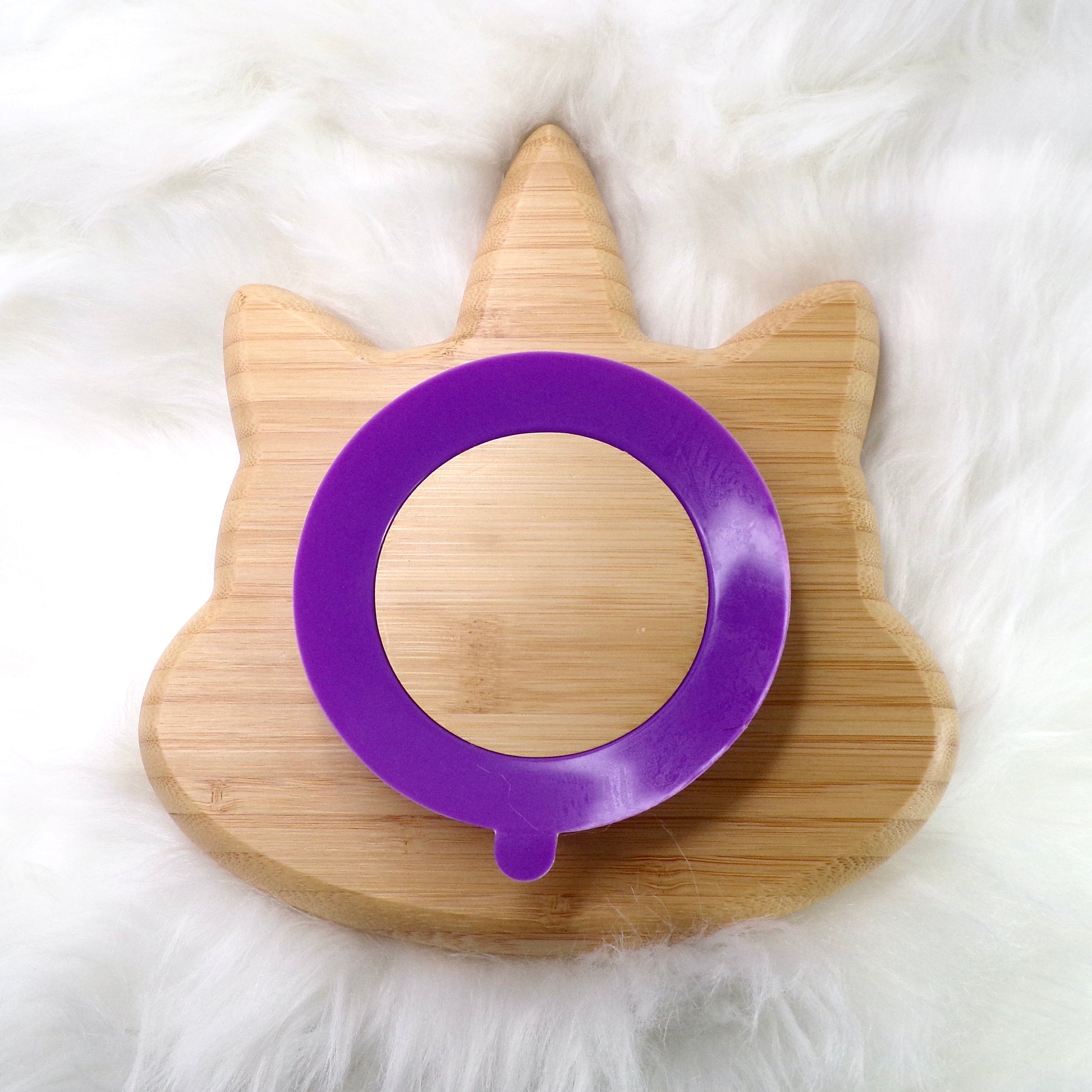 A bamboo children’s plate, with multiple food sections, in a unicorn design. The bamboo plate features a purple silicone suction ring at the back, and includes bamboo fork and spoon utensils in matching colours. Back view.