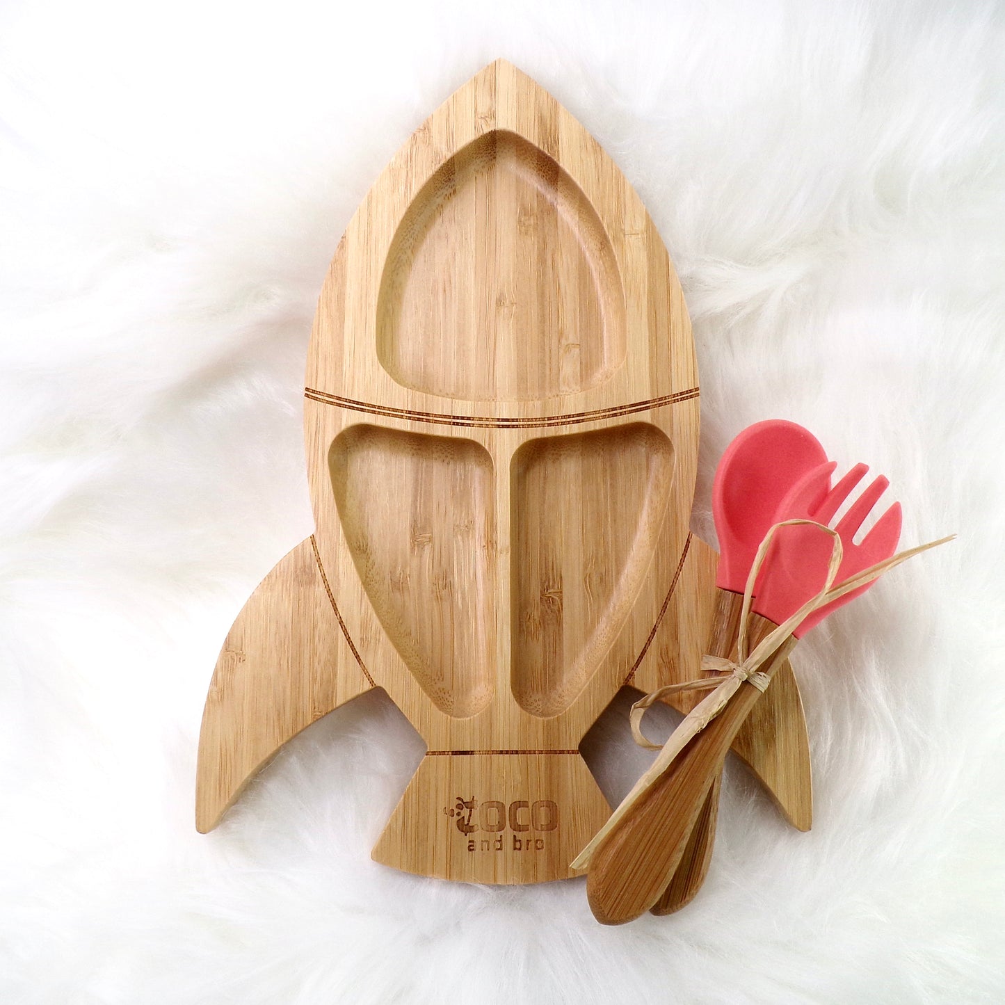 A children's bamboo section plate with a rocket design, coral colour silicone suction ring and matching coral colour bamboo and silicone cutlery. Front view.