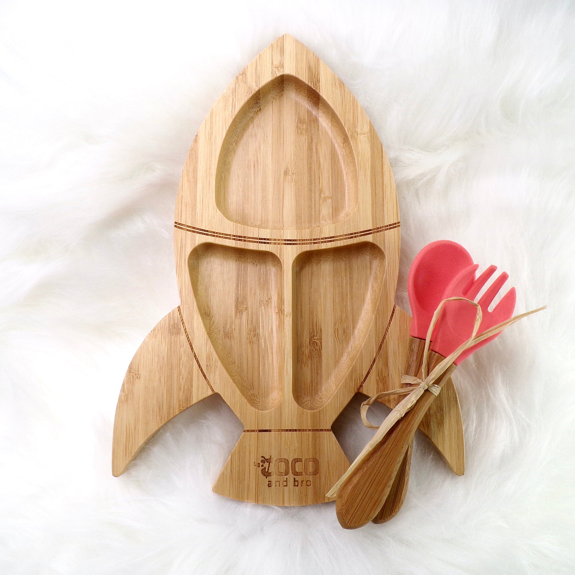 A children's bamboo section plate with a rocket design, coral colour silicone suction ring and matching coral colour bamboo and silicone cutlery. Front view.