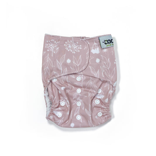An adjustable reusable nappy for babies and toddlers, featuring a floral lilac design, with floral images on a lilac background. View shows the front of the nappy, with fastenings closed.