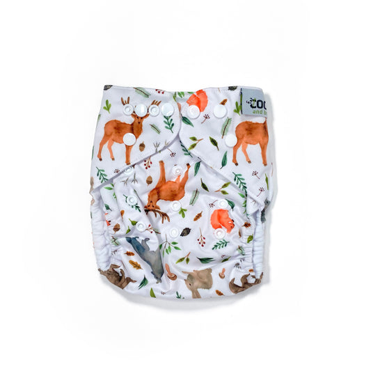 An adjustable reusable nappy for babies and toddlers, featuring a woodland animal design, with images of various woodland animals on a white background. View shows the front of the nappy, with fastenings closed.