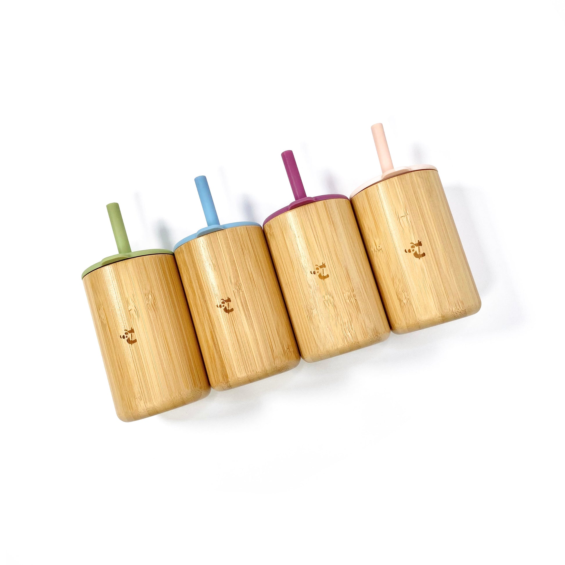 A collection of children’s bamboo drinking cups, with colourful silicone lids and matching straws. View shows the cups from above, arranged in a line displaying the Coco and Bro logos.