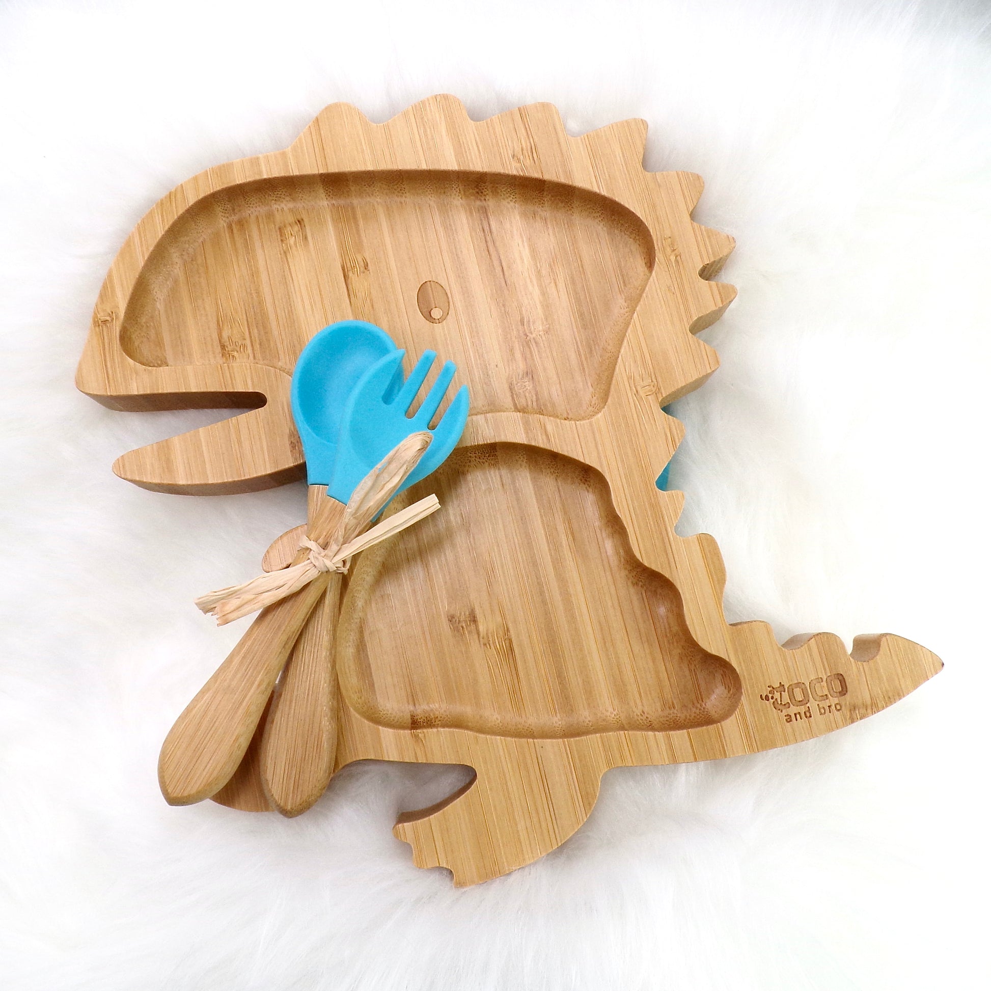A children's bamboo section plate with a dinosaur design, blue silicone suction ring and matching blue bamboo and silicone cutlery. Front view.