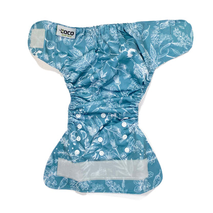 An adjustable reusable nappy for babies and toddlers, featuring a blue harvest design, with white images of various crops on a blue background. View shows the full outside pattern of the nappy, with fastenings open.