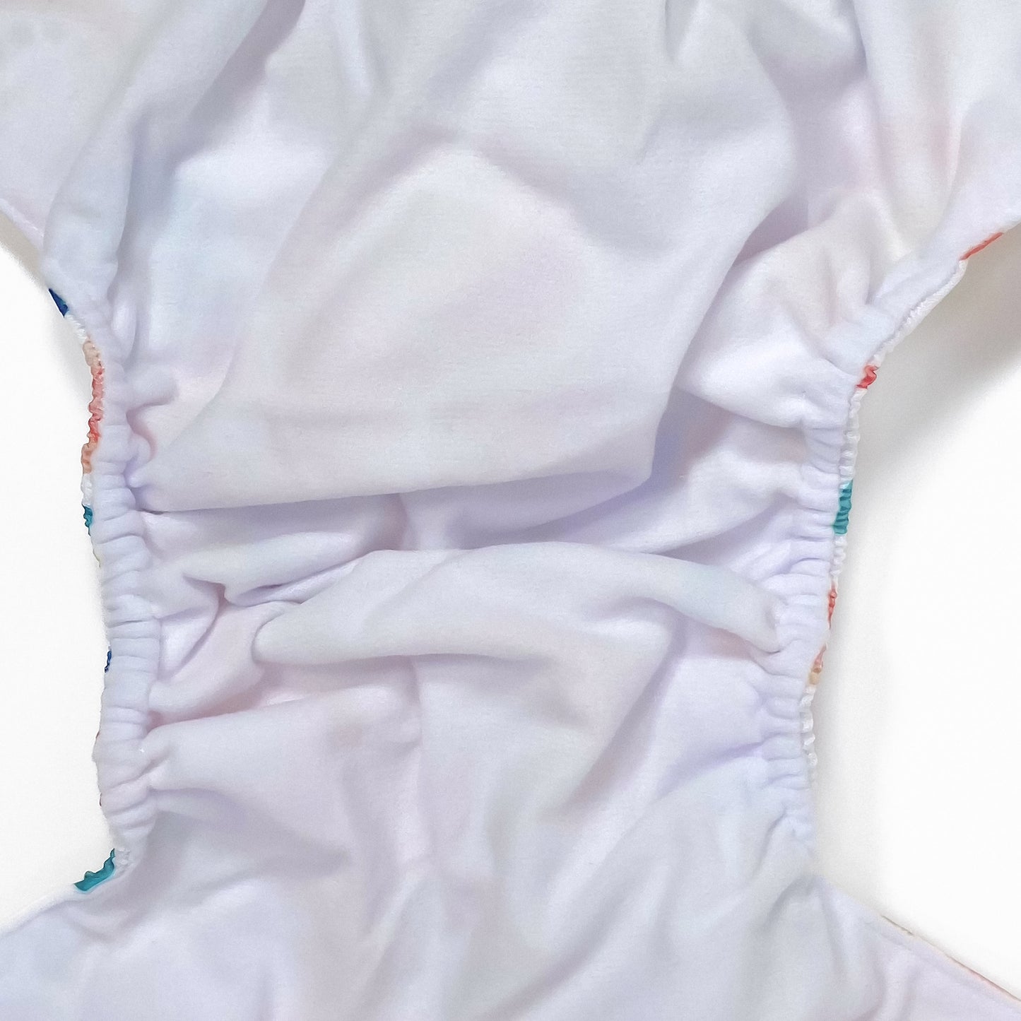 An adjustable reusable nappy for babies and toddlers, featuring a bright rainbow design, with brightly coloured rainbows on a white background. Image shows a zoomed in view of the nappy fabric lining.