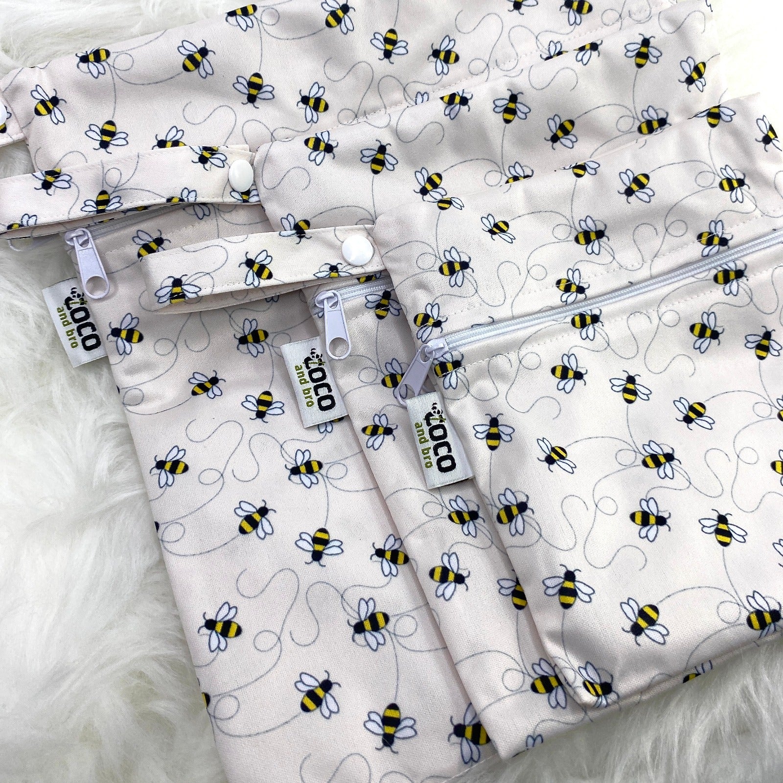A set of three waterproof bags in an off-white bumble bee design, made from bamboo and in three different sizes. Each bag has a zipper closure.