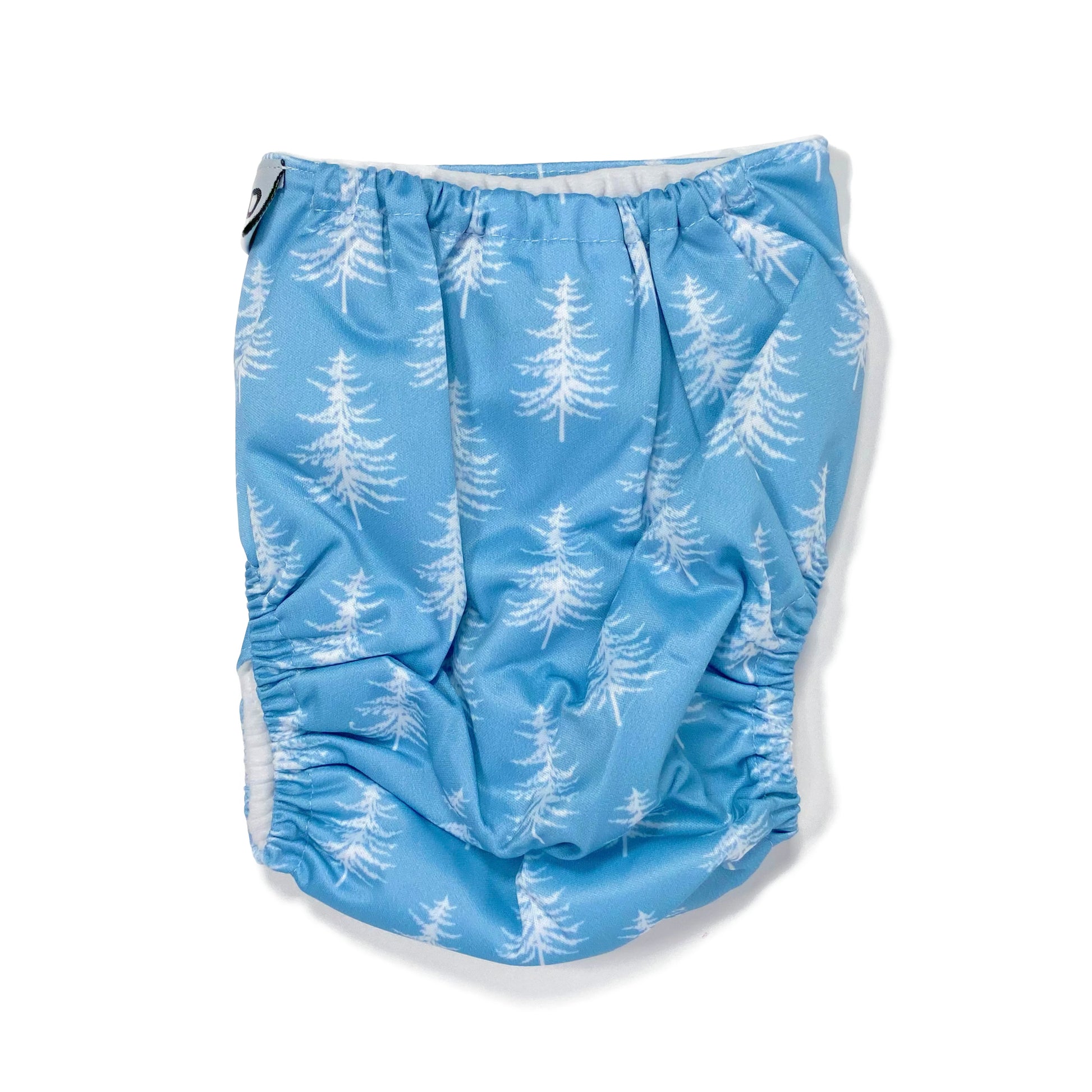 An adjustable reusable nappy for babies and toddlers, featuring a cool blue pine design design, with images of white pine trees on a blue background. View shows the back of the nappy.