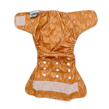 An adjustable reusable nappy for babies and toddlers, featuring a floral copper design, with floral images on a copper background. View shows the full outside pattern of the nappy, with fastenings open.