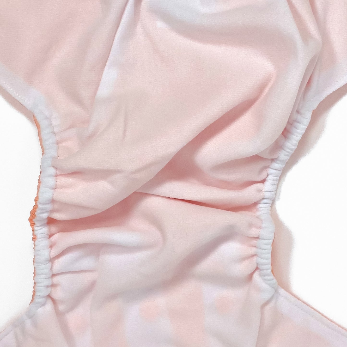An adjustable reusable nappy for babies and toddlers, in a bright coral colour. Image shows a zoomed in view of the nappy fabric lining.