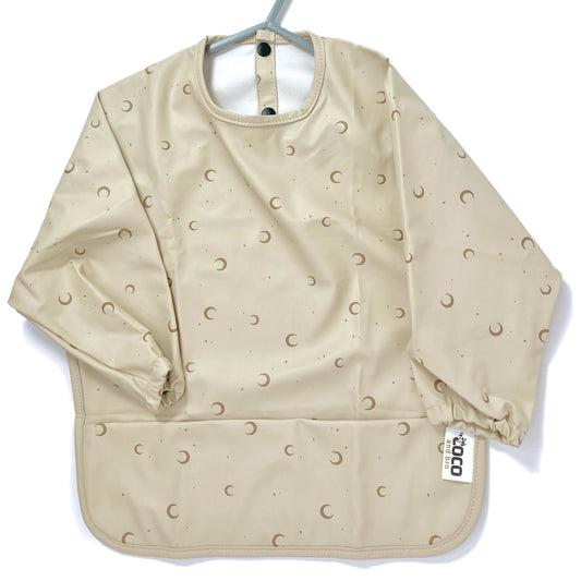 Long-sleeve kids apron in a beige and moon design, showing front view.
