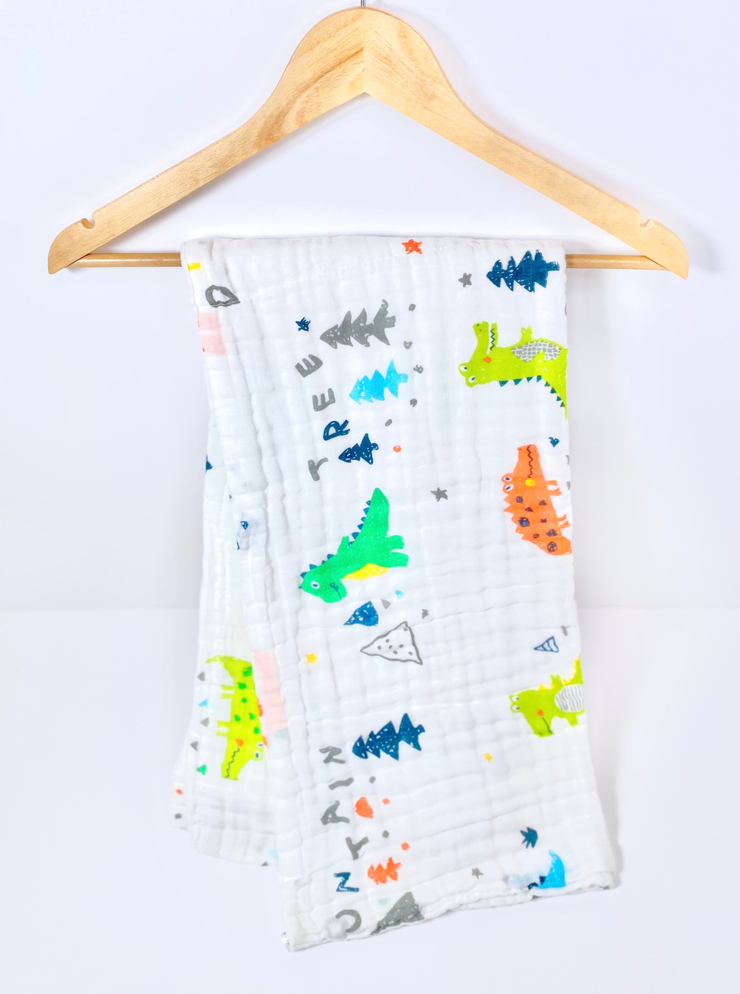 A muslin baby buggy blanket made from bamboo and cotton fibres, in a dinosaur crocodile design.