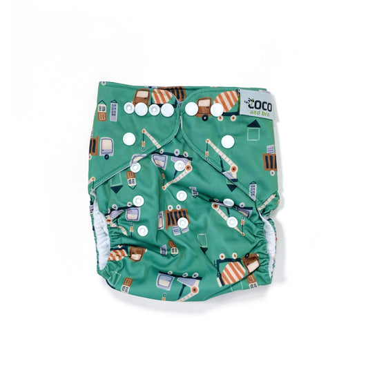 An adjustable reusable nappy for babies and toddlers, featuring a green construction design, with images of construction vehicles on a green background. View shows the front of the nappy, with fastenings closed.