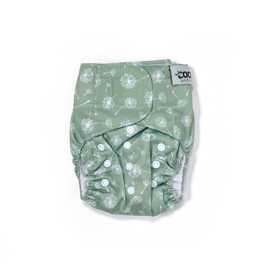 An adjustable reusable nappy for babies and toddlers, featuring a green dandelion design, with images of dandelion seeds on a green background. View shows the front of the nappy, with fastenings closed.