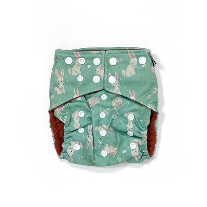 An adjustable reusable nappy for babies and toddlers, featuring a green rabbits design, with images of grey rabbits on a green background. 