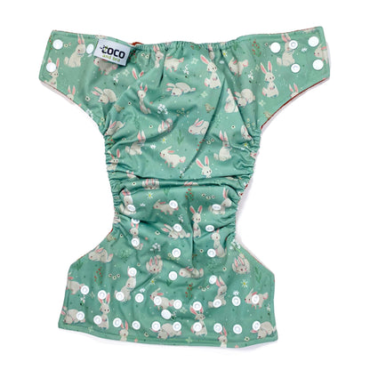 An adjustable reusable nappy for babies and toddlers, featuring a green rabbits design, with images of grey rabbits on a green background. View shows the full outside pattern of the nappy, with fastenings open.