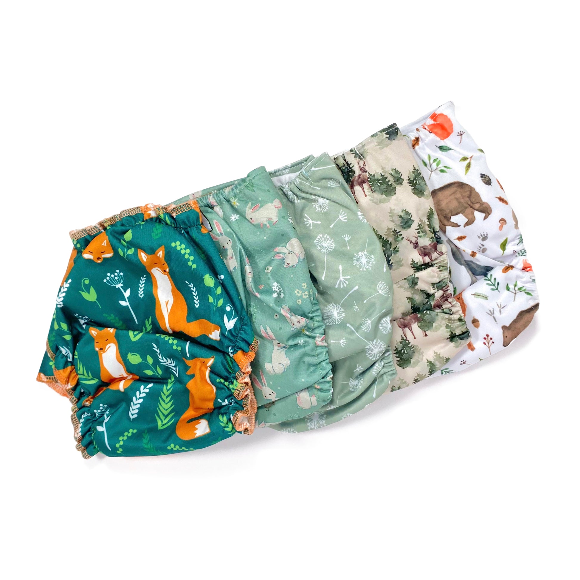 A set of five reusable nappies, made from 100% recycled polyester. The included nappies are: Woodland Friends, Winter Forest, Green Dandelion, Green Rabbits and Green Fox. View shows all five nappies back facing, in a diagonal line.