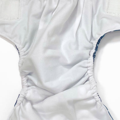 An adjustable reusable nappy for babies and toddlers, featuring a midnight breeze design, with images of dandelion seeds on a navy blue background. Image shows a zoomed in view of the nappy fabric lining.