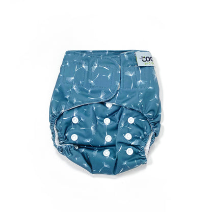 An adjustable reusable nappy for babies and toddlers, featuring a midnight breeze design, with images of dandelion seeds on a navy blue background. View shows the front of the nappy, with fastenings closed.