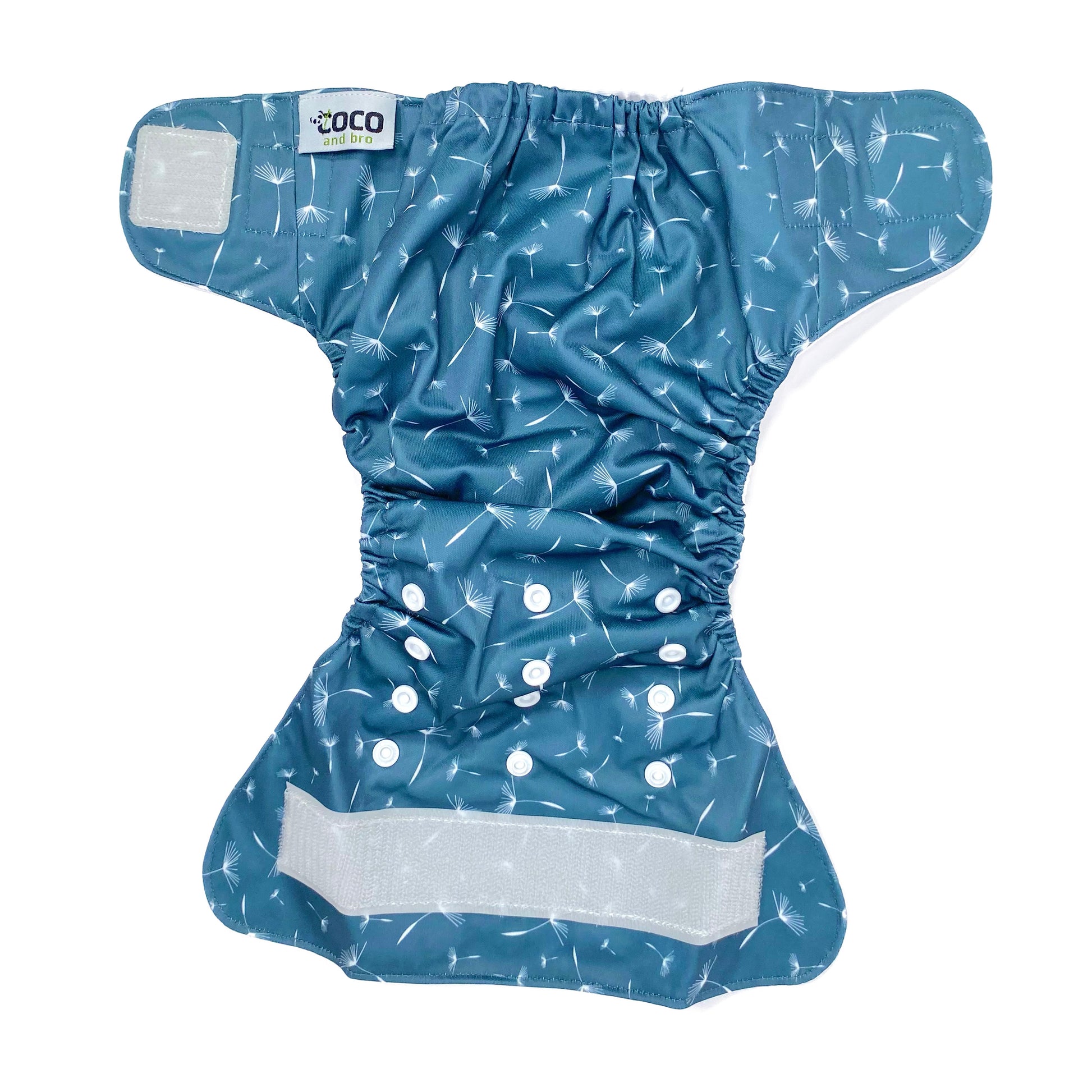 An adjustable reusable nappy for babies and toddlers, featuring a midnight breeze design, with images of dandelion seeds on a navy blue background. View shows the full outside pattern of the nappy, with fastenings open.