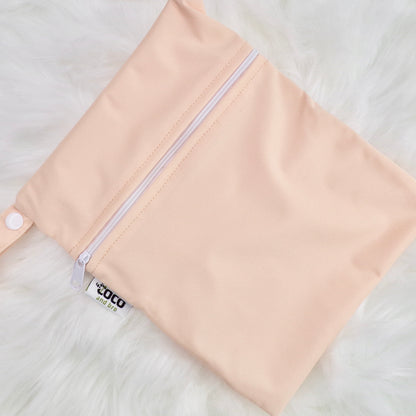 Each backpack purchase includes a free waterproof bag. This image shows the waterproof bag in peachy pink, with a zip closure.