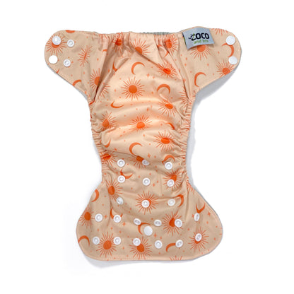 An adjustable reusable nappy for babies and toddlers, featuring a peach cosmos design, with images of moons, suns and stars on a peach background. View shows the full outside pattern of the nappy, with fastenings open.