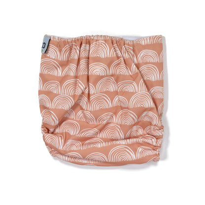 An adjustable reusable nappy for babies and toddlers, featuring a peach rainbow design, with images of white rainbows on a peach background. View shows the back of the nappy.