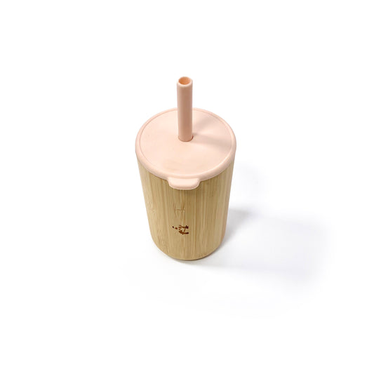 A children’s bamboo drinking cup, with a peachy pink silicone lid and matching straw. View shows the cup with lid and straw attached.