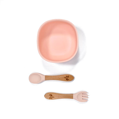 A peachy pink silicone children’s feeding bowl, with matching bamboo and silicone cutlery.