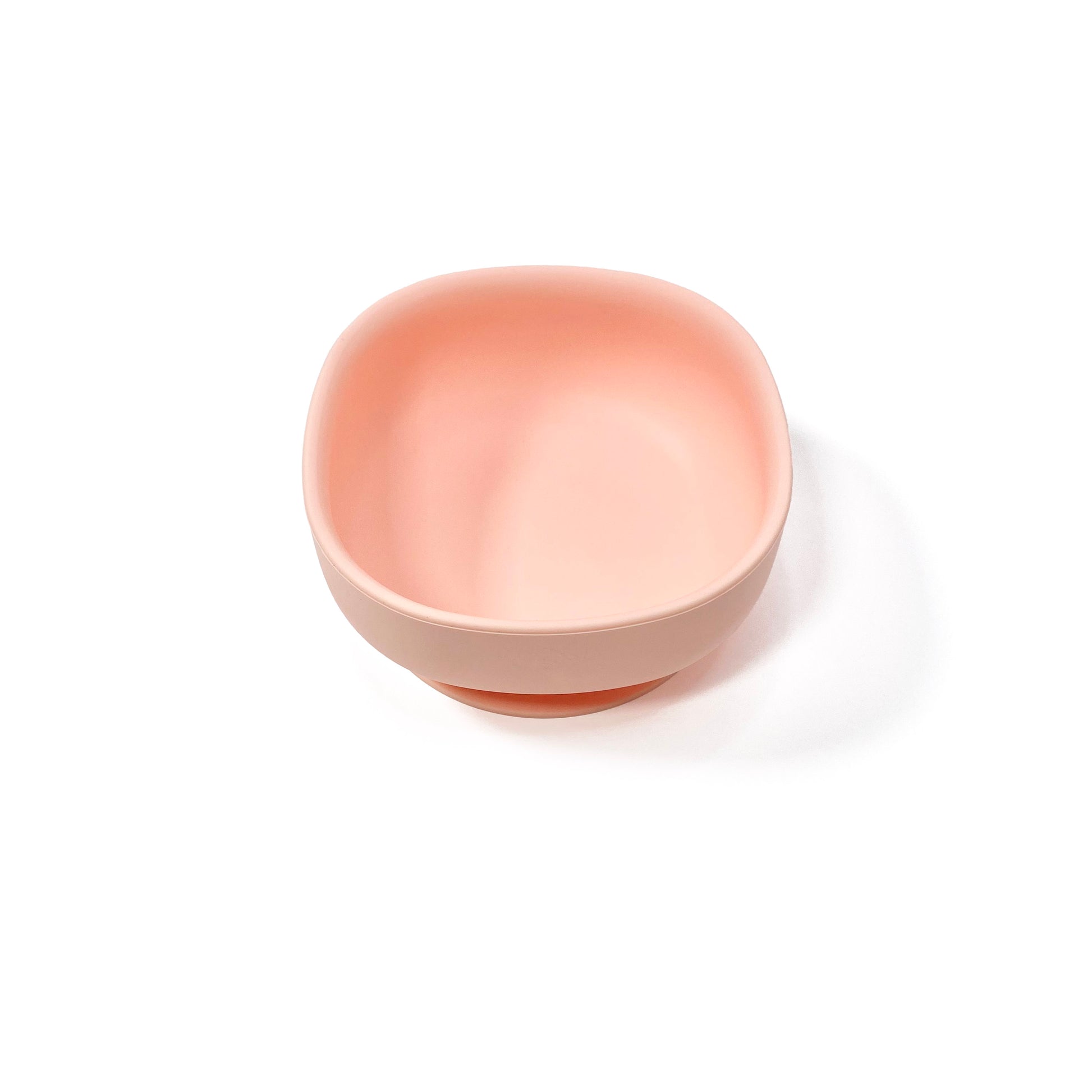 A peachy pink silicone children’s feeding bowl with suction cup on the base. Side view.