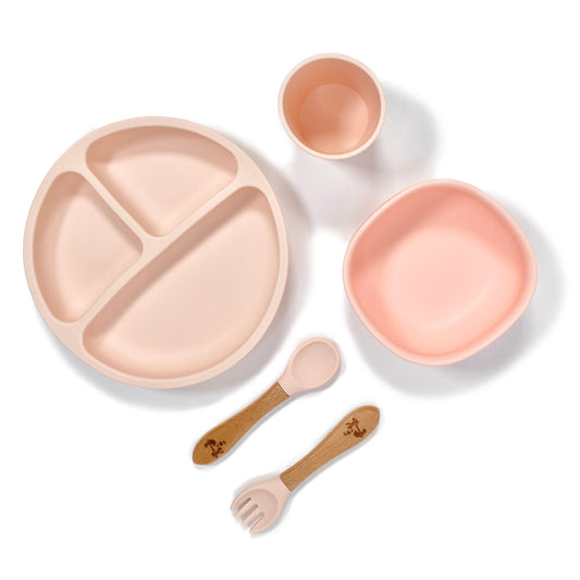 A peachy pink silicone children’s feeding set, comprised of silicone section plate with suction cups, silicone bowl with suction cup, silicone drinking cup and matching bamboo and silicone cutlery.