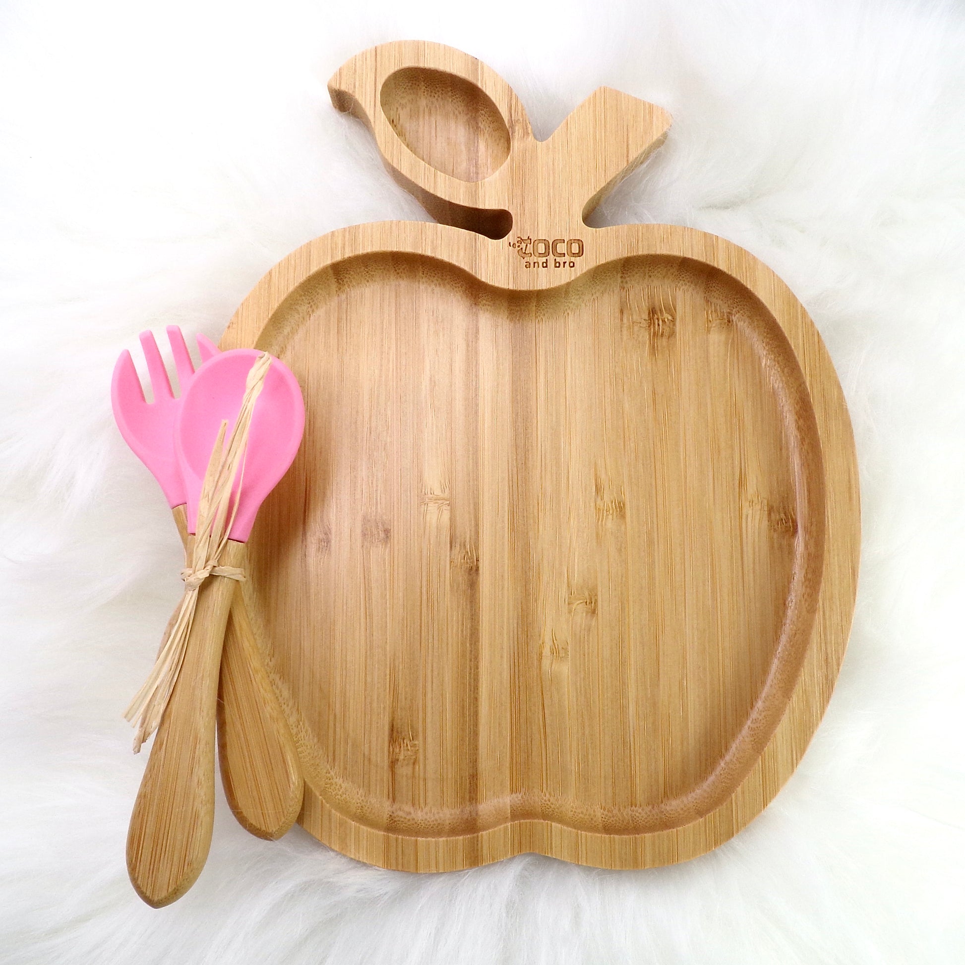 A bamboo children’s plate, with multiple food sections, in an apple design. The bamboo plate features a pink silicone suction ring at the back, and includes bamboo fork and spoon utensils in matching colours. Front view.