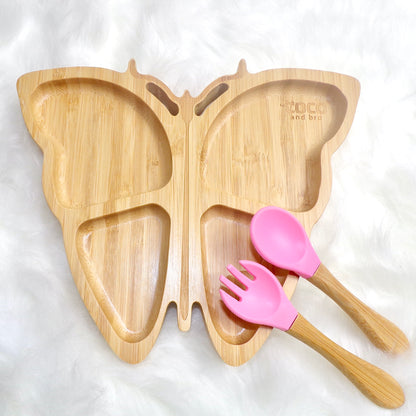 A children's bamboo section plate with a butterfly design, pink colour silicone suction ring and matching pink bamboo and silicone cutlery. Front view.