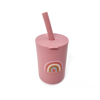 A children’s pink silicone drinking cup, with matching lid and straw, featuring a rainbow design. The image shows the cup with lid and straw attached.