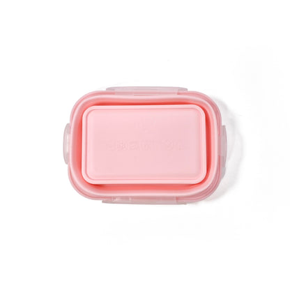 A collapsible pink rectangular silicone food storage tub with lid. View shows the underside of the tub, with the tub fully collapsed.
