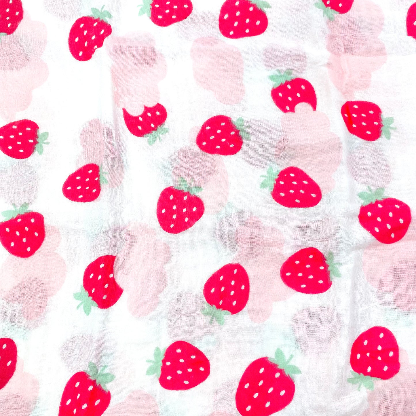 A close up view of the pink strawberry pattern of a muslin baby blanket.