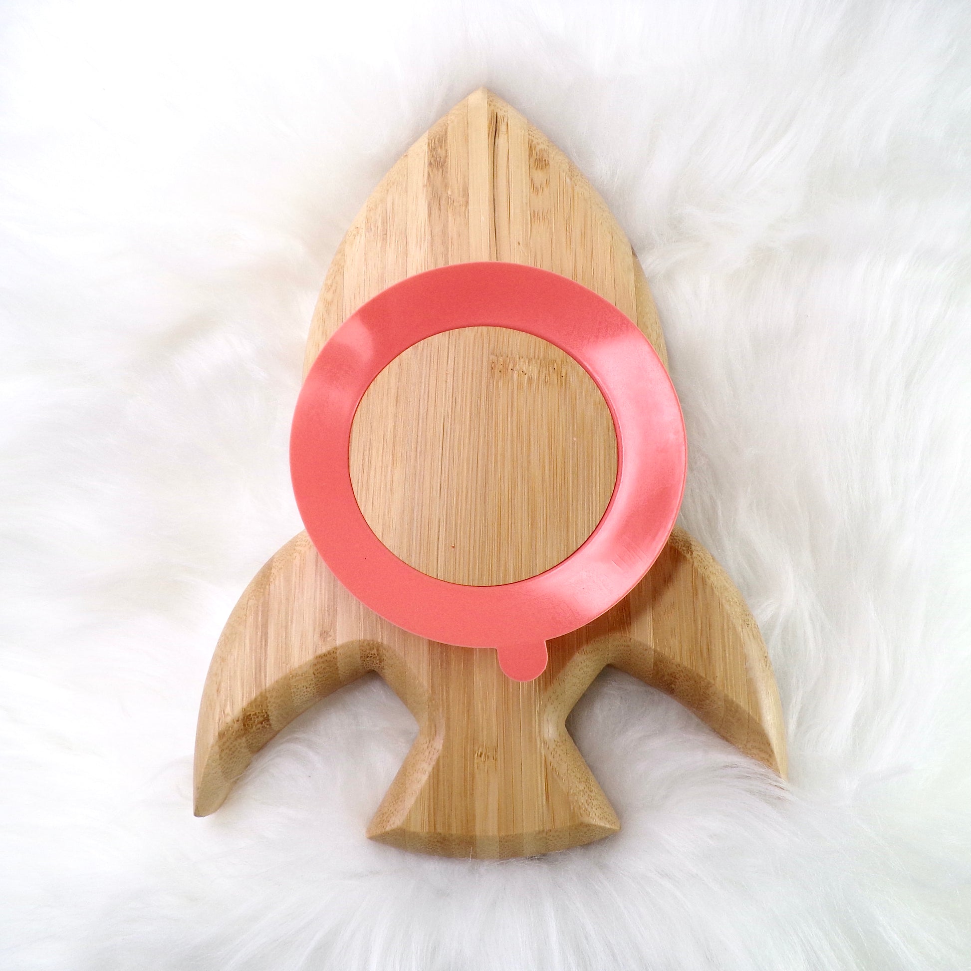 A children's bamboo section plate with a rocket design, coral colour silicone suction ring and matching coral colour bamboo and silicone cutlery. Front view.