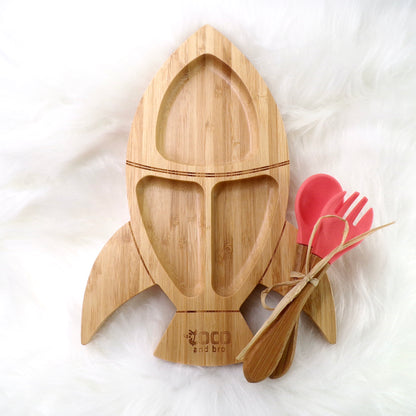 A children's bamboo section plate with a rocket design, coral colour silicone suction ring and matching coral colour bamboo and silicone cutlery. Front view.