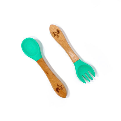 A set of children’s bamboo and silicone cutlery, in seafoam green. The set is comprised of a fork and spoon.