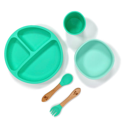 A seafoam green silicone children’s feeding set, comprised of silicone section plate with suction cups, silicone bowl with suction cup, silicone drinking cup and matching bamboo and silicone cutlery.