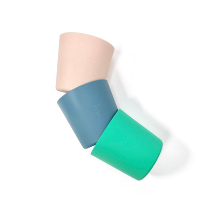 A collection of silicone children’s cups, available in peachy pink, ocean blue and seafoam green. The cups are shown connected in a semi-circle, from above.