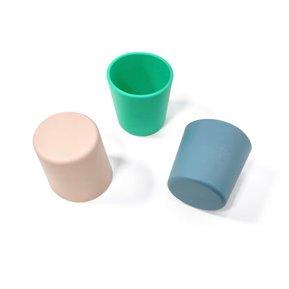 A collection of silicone children’s cups, available in peachy pink, ocean blue and seafoam green. The cups are shown in a scattered formation.